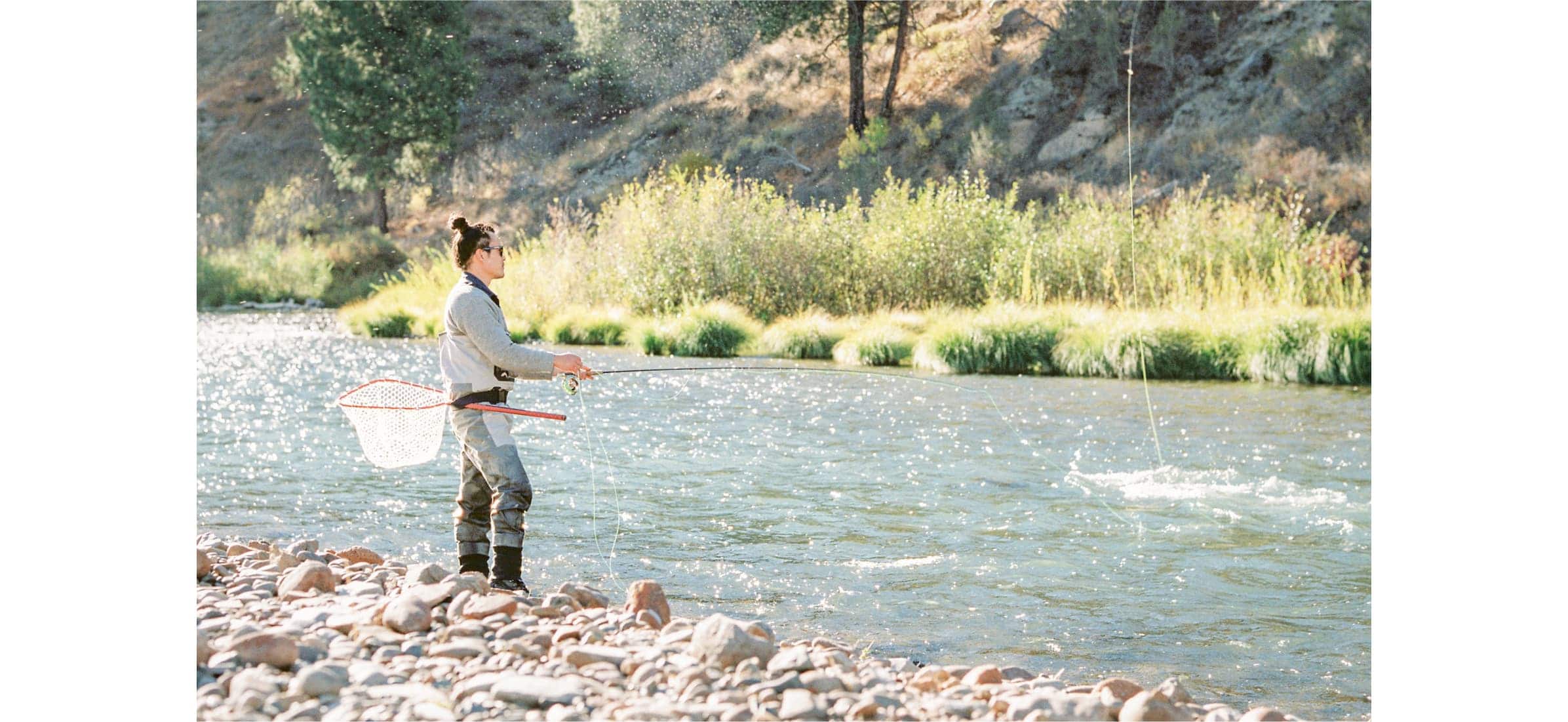 Burton stands at the edge of a sunlit river fishing.